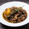 Close-up of savory Caribbean oxtail stew with potatoes served on a white plate.